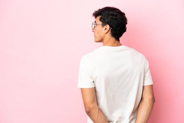 Young Argentinian man isolated on pink background in back position and looking back