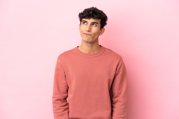 Young Argentinian man isolated on pink background having doubts while looking up