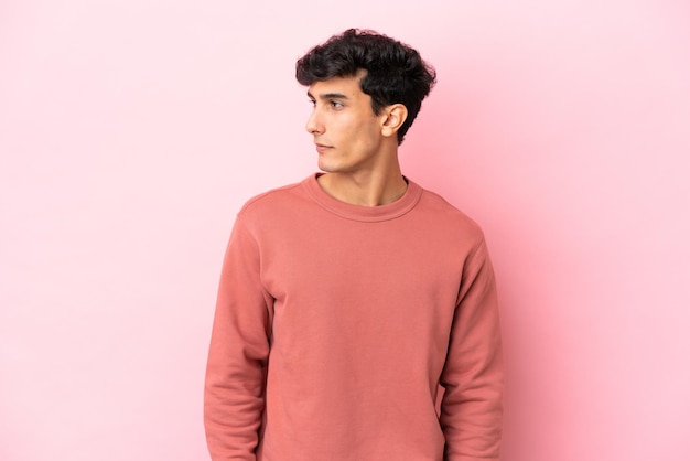 Young Argentinian man isolated on pink background looking to the side