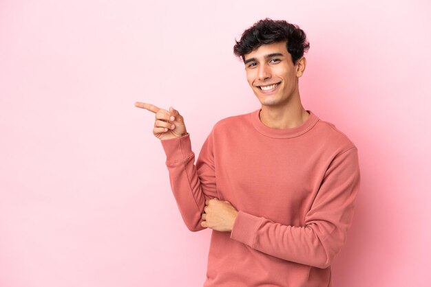 Young Argentinian man isolated on pink background pointing finger to the side