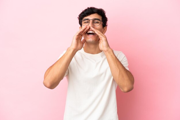 Young Argentinian man isolated on pink background shouting and announcing something