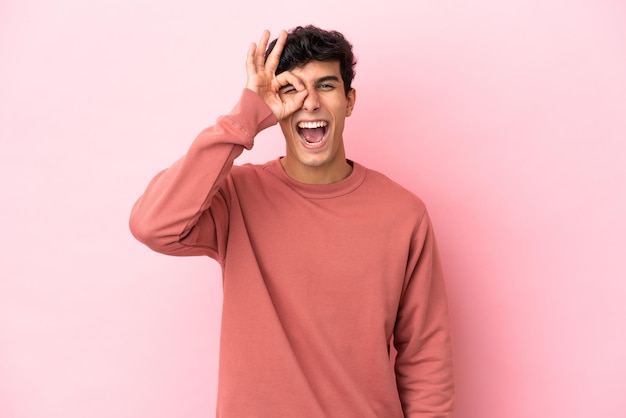 Giovane uomo argentino isolato su sfondo rosa che mostra segno ok con le dita