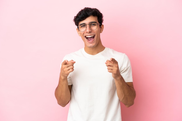 Young Argentinian man isolated on pink background surprised and pointing front