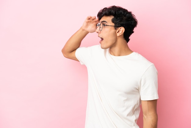 Young Argentinian man isolated on pink background with surprise expression while looking side