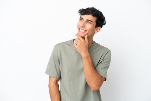 Young Argentinian man isolated on white background looking up while smiling