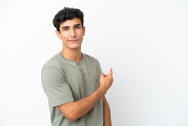 Young Argentinian man isolated on white background pointing back