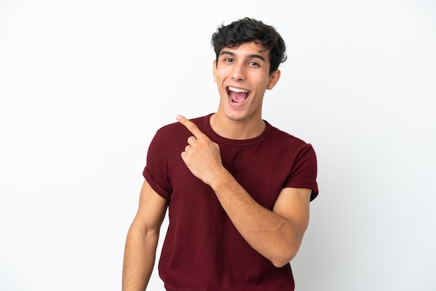 Young Argentinian man isolated on white background surprised and pointing side