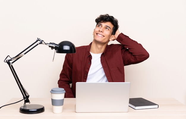 Молодой аргентинский мужчина в таблице с ноутбуком на своем рабочем месте смеется