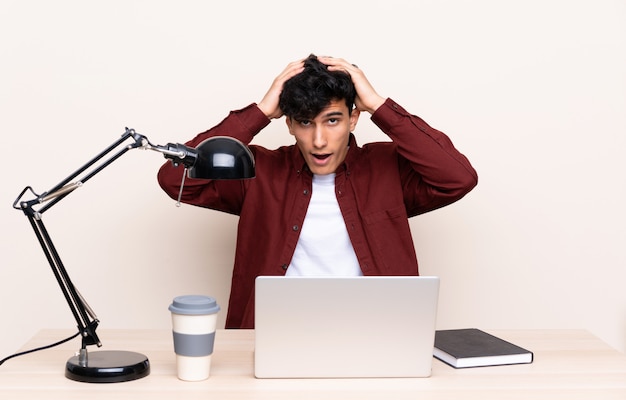 Young Argentinian man in a table with a laptop in his workplace with surprise facial expression