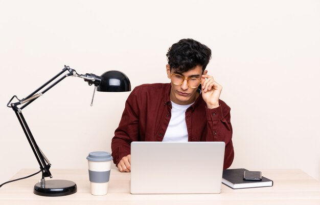 Young Argentinian man in a table with a laptop in his workplace