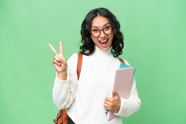 孤立した背景の上で笑顔で勝利のサインを示す若いアルゼンチンの学生女性