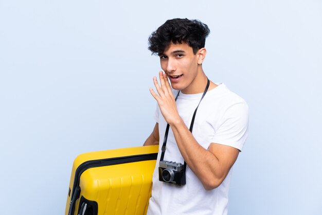 Young Argentinian traveller man over isolated blue wall whispering something