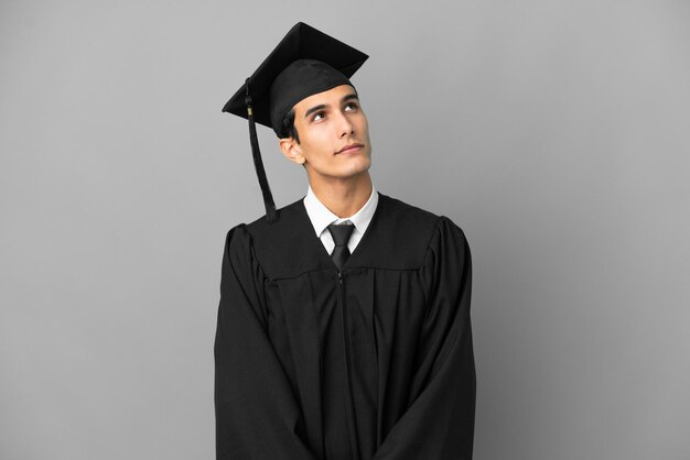 Giovane laureato argentino isolato su sfondo grigio e alzando lo sguardo Foto Premium