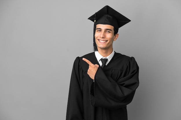 Young argentinian university graduate isolated on grey\
background pointing to the side to present a product