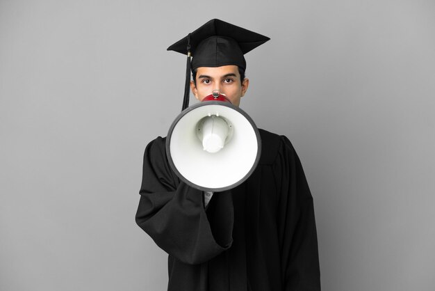 Young Argentinian university graduate isolated on grey background shouting through a megaphone