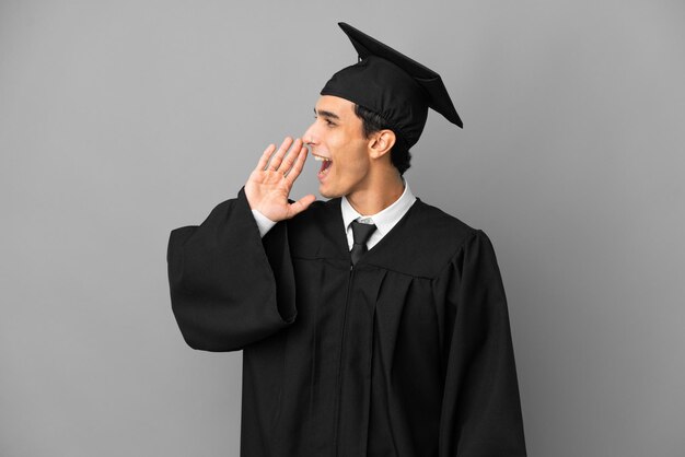 Young Argentinian university graduate isolated on grey background shouting with mouth wide open to the lateral