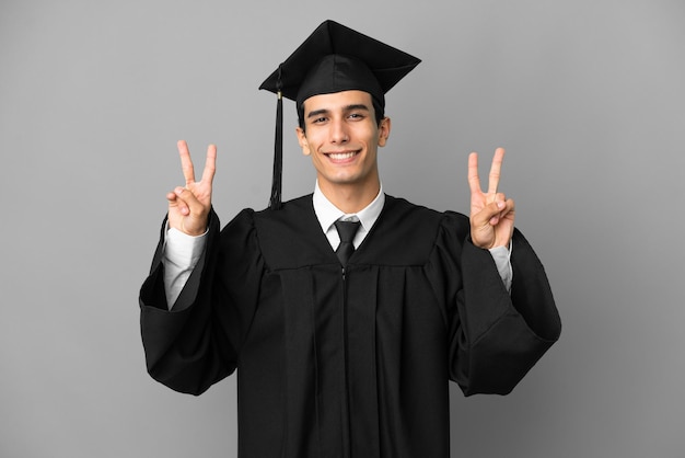 Young Argentinian university graduate isolated on grey background showing victory sign with both hands