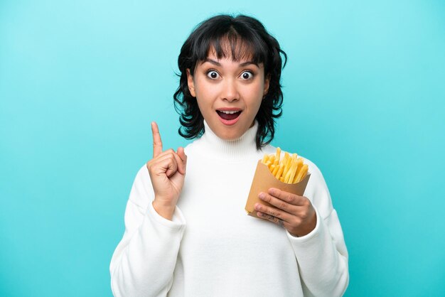 Giovane donna argentina che tiene patatine fritte isolate su sfondo blu con l'intenzione di realizzare la soluzione sollevando un dito