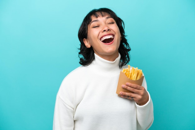 Young Argentinian woman holding fried chips isolated on blue background laughing