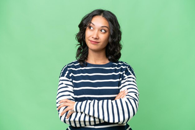 Young Argentinian woman over isolated background looking up while smiling