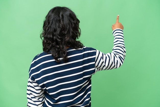 Молодая аргентинская женщина на изолированном фоне показывает указательным пальцем назад