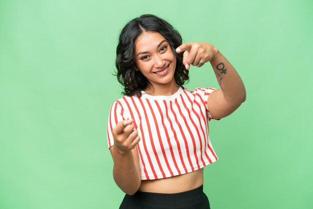 Young Argentinian woman over isolated background points finger at you while smiling