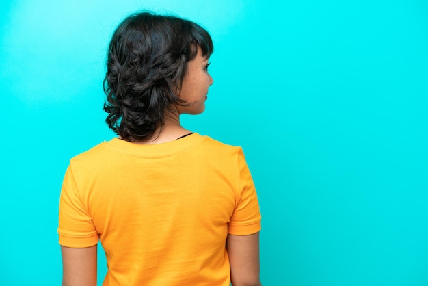 Young Argentinian woman isolated on blue background in back position and looking side