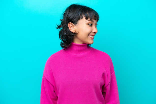 Young Argentinian woman isolated on blue background looking to the side