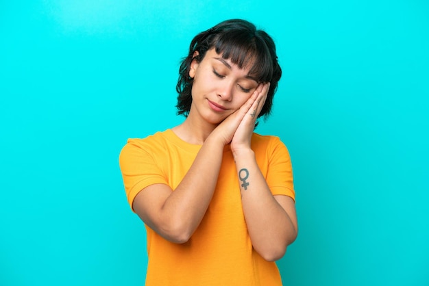 Young Argentinian woman isolated on blue background making sleep gesture in dorable expression