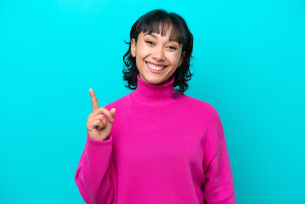 Young Argentinian woman isolated on blue background showing and lifting a finger in sign of the best