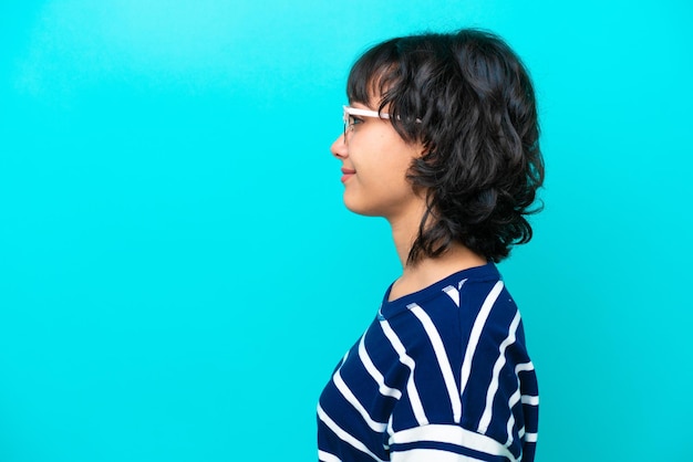 Young Argentinian woman isolated on blue background With glasses