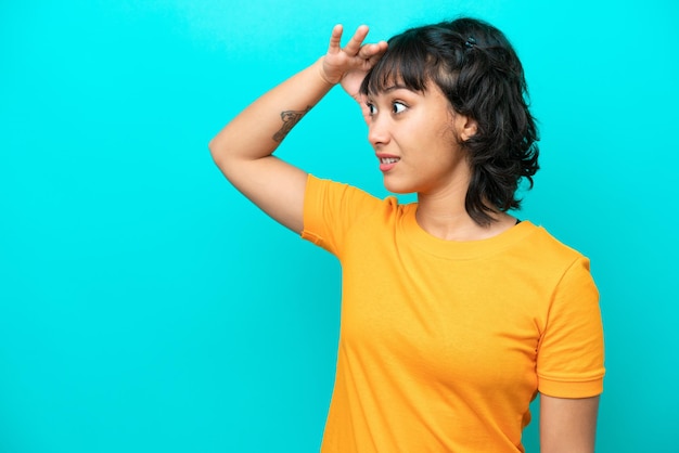 Young Argentinian woman isolated on blue background with surprise expression while looking side