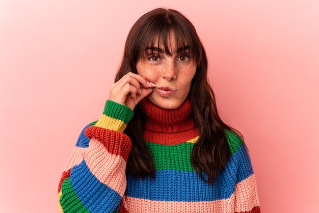 Young Argentinian woman isolated on pink background with fingers on lips keeping a secret.