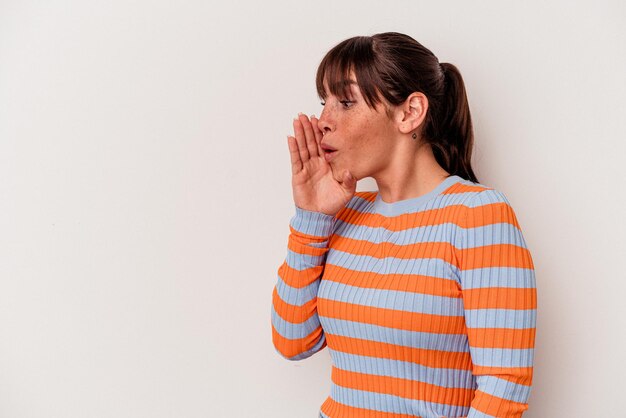 Young Argentinian woman isolated on white background is saying a secret hot braking news and looking aside