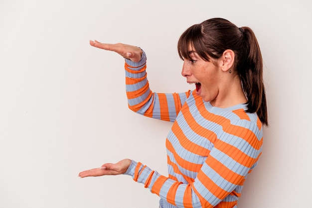 Young Argentinian woman isolated on white background shocked and amazed holding a copy space between hands.