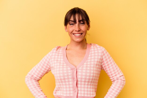 Young Argentinian woman isolated on yellow background confident keeping hands on hips.