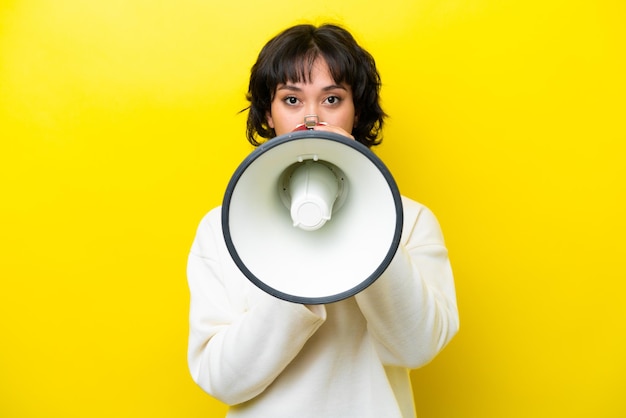 Young argentinian woman isolated on yellow background shouting through a megaphone to announce something
