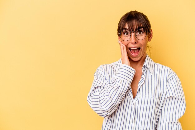 Young Argentinian woman isolated on yellow background shouts loud, keeps eyes opened and hands tense.