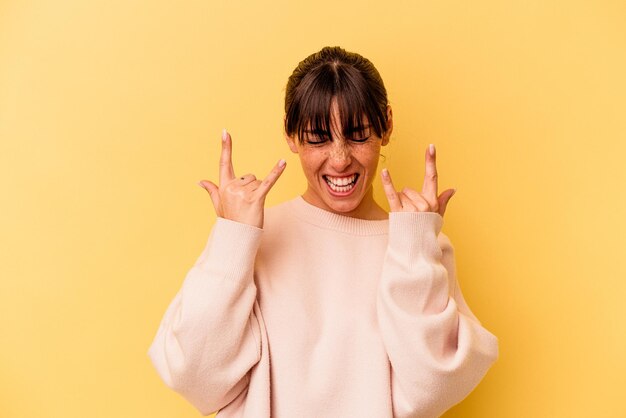 Young Argentinian woman isolated on yellow background showing a horns gesture as a revolution concept.