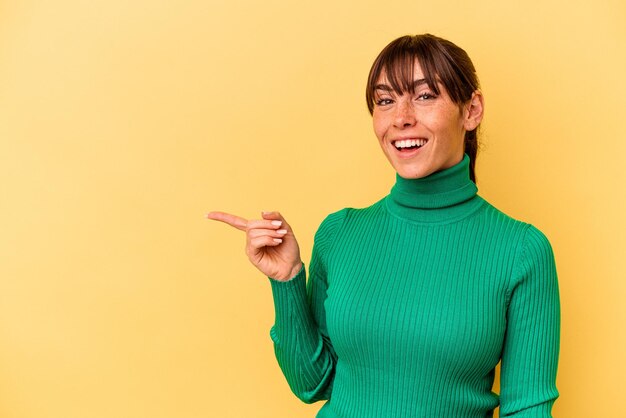 Young Argentinian woman isolated on yellow background smiling cheerfully pointing with forefinger away.