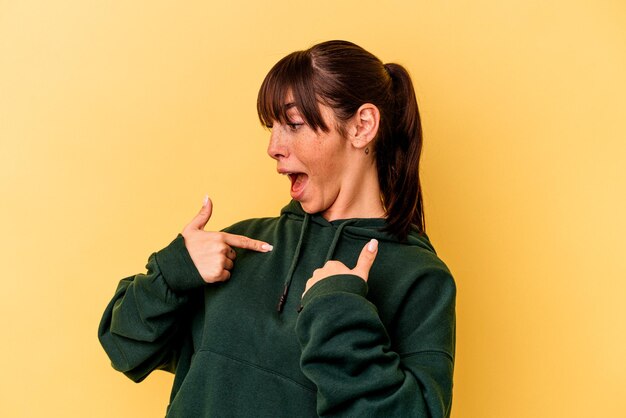 Young Argentinian woman isolated on yellow background surprised pointing with finger, smiling broadly.