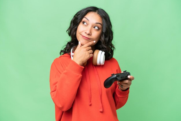 Young Argentinian woman playing with a video game controller over isolated background and looking up