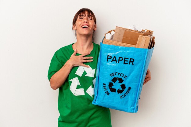 Young Argentinian woman recycled paper isolated on yellow background laughs out loudly keeping hand on chest.