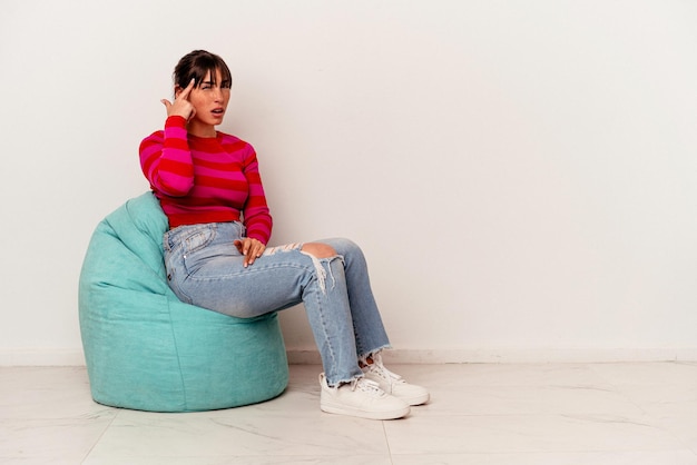 Young Argentinian woman sitting on a puff isolated on white background showing a disappointment gesture with forefinger.