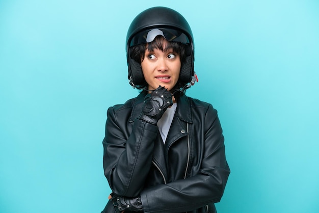 사진 푸른 배경에 오토바이 헬멧을 쓴 젊은 아르헨티나 여성이 의심과 생각을 가지고 있다