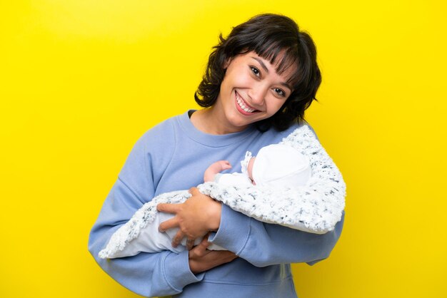 Young Argentinian woman with her cute baby isolated on yellow background