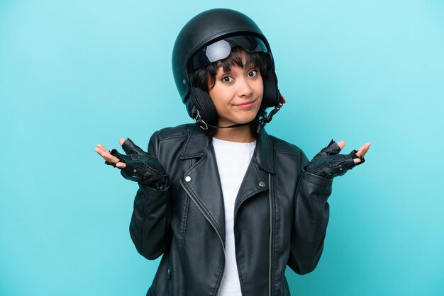 Young Argentinian woman with a motorcycle helmet isolated on blue background having doubts while raising hands