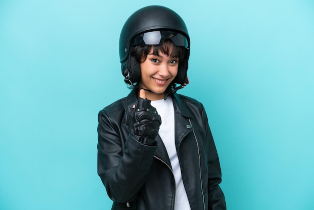 Young argentinian woman with a motorcycle helmet isolated on\
blue background inviting to come with hand happy that you came