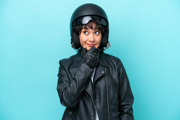 Young Argentinian woman with a motorcycle helmet isolated on blue background looking up while smiling