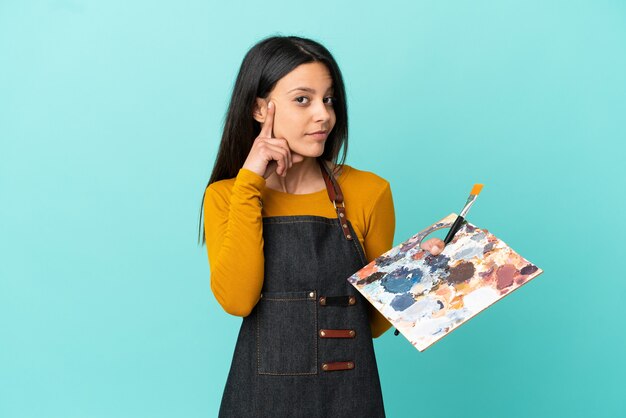 Young artist caucasian woman holding a palette isolated on blue background thinking an idea